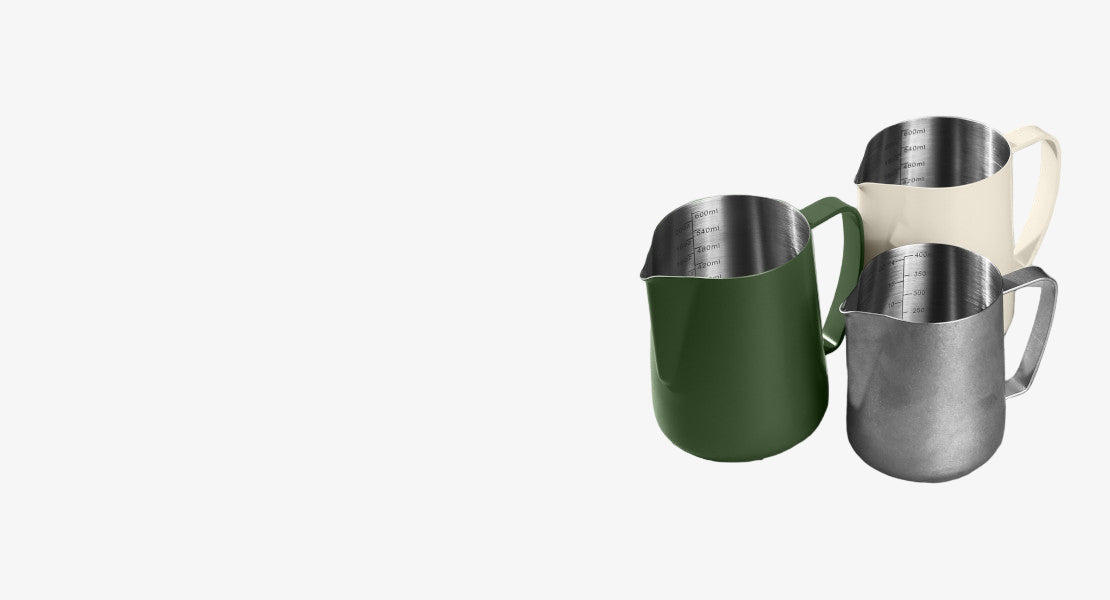 Three stainless steel pitchers in green, silver, and beige on a light gray surface.